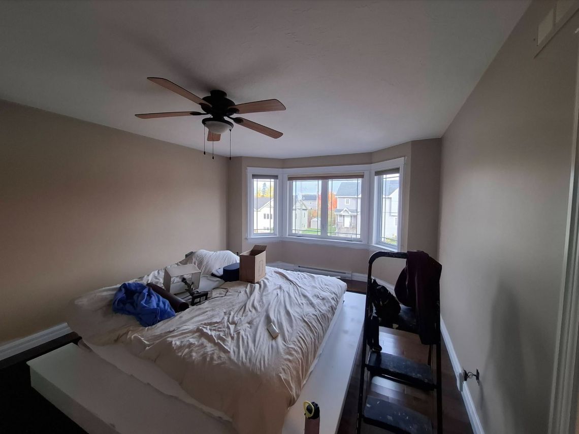 Bedroom walls with white trim, furniture covered during painting